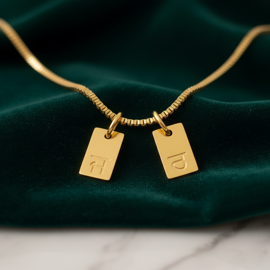 Gold-plated initial tag necklace with Gurmukhi letters, two tags on green velvet