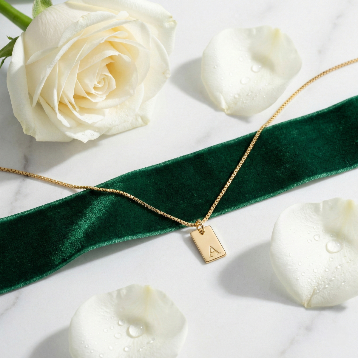 Dainty initial tag necklace, gold-tone rectangular tag with letter 'A', on marble with white rose petals