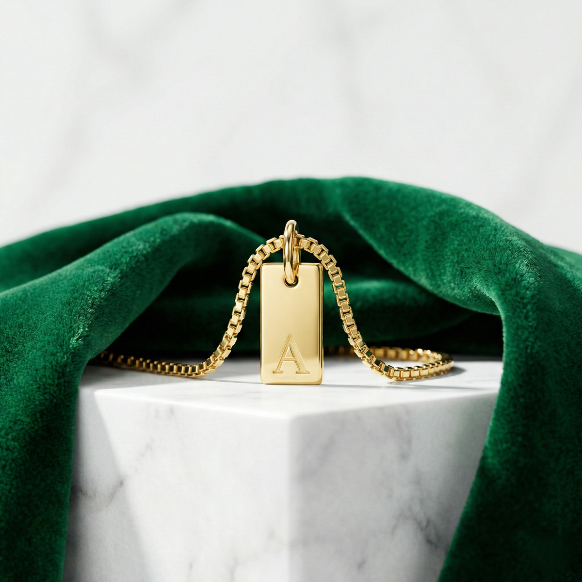 Dainty initial tag necklace, gold-tone rectangular tag with letter 'A', on a marble block with velvet