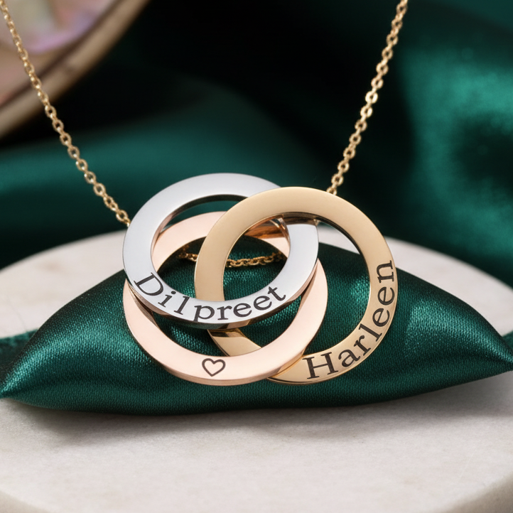 Linked circles necklace: three interlocking rings engraved with names such as 'Dilpreet' and 'Harleen', on a velvet cushion on marble