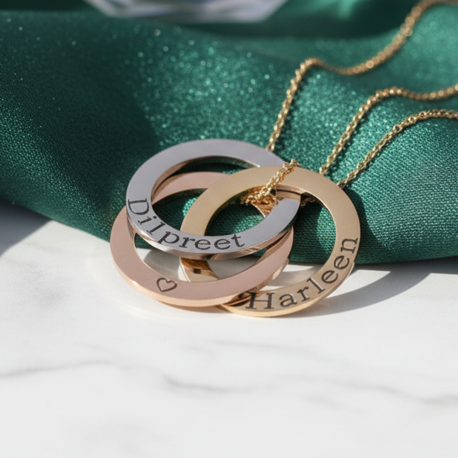 Linked circles necklace: three interlocking rings engraved with names such as 'Dilpreet' and 'Harleen', on a velvet cushion with marble