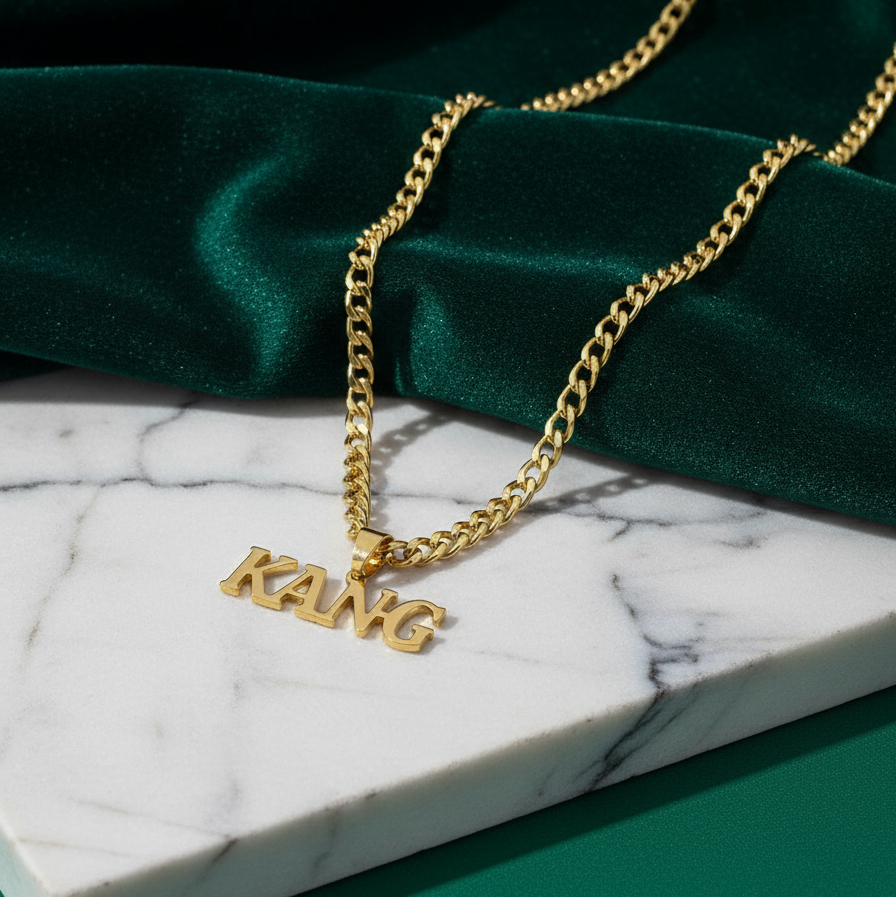 Gold-plated custom name necklace for men on a curb chain, name 'KANG' in English lying on marble