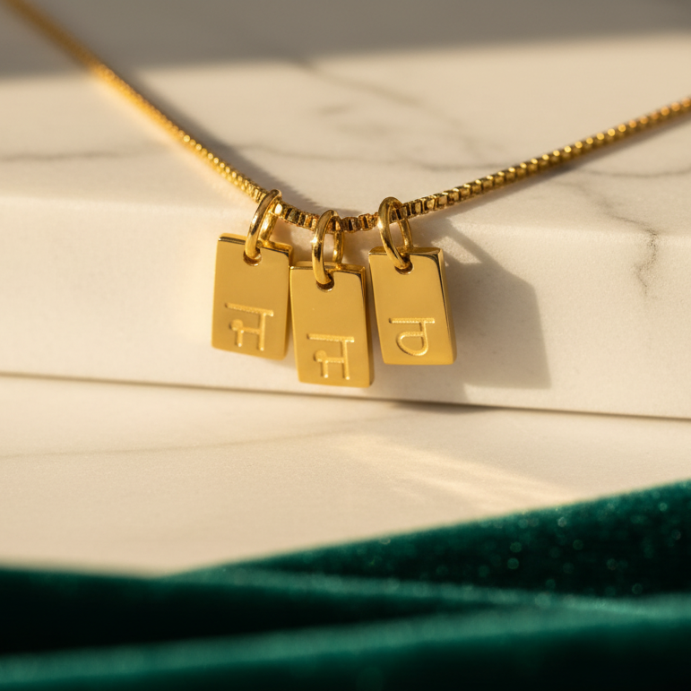 Gold-plated initial tag necklace with Gurmukhi letters, three tags on marble