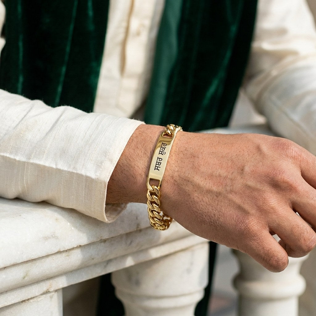 Gold curb name bracelet on a man's wrist with a cream kurta