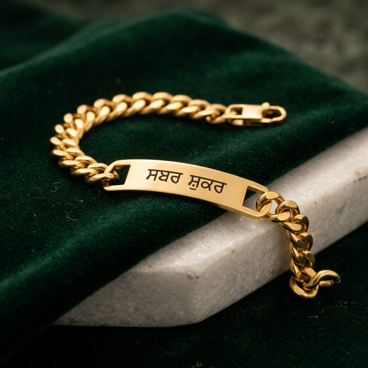 Open gold curb name bracelet with ਸਬਰ ਸ਼ੁਕਰ on green velvet and white marble