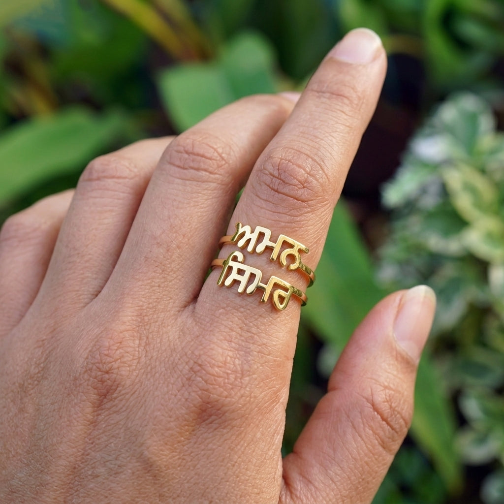 Gold double name ring with Punjabi names Aman and Simar worn on the finger