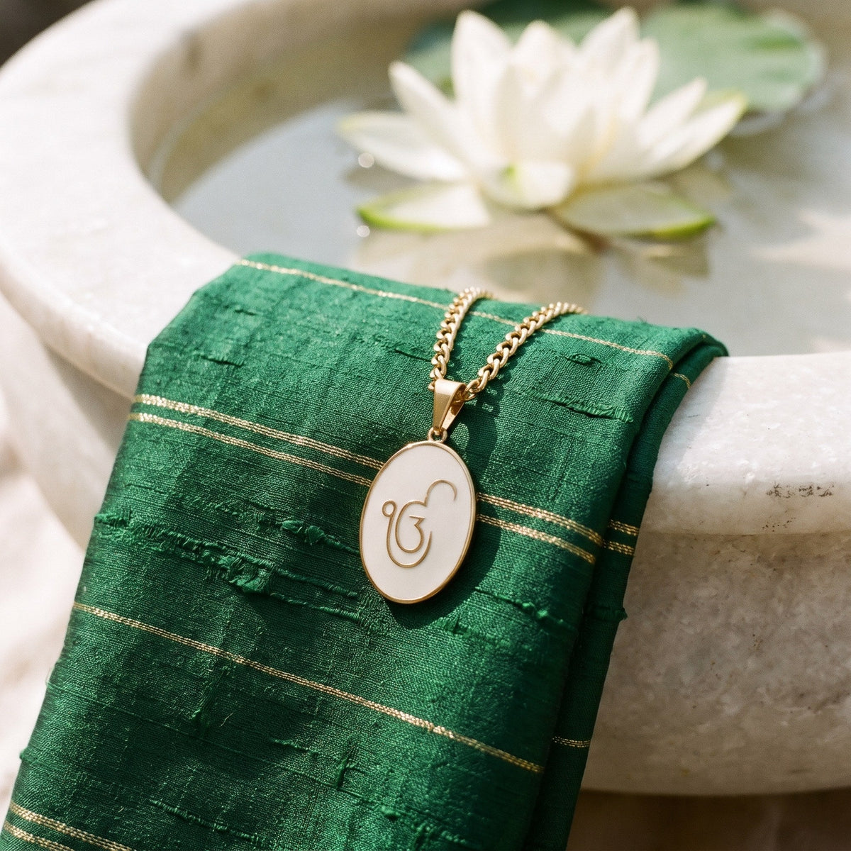 Ik Onkar enamel pendant on green silk beside a marble bowl with a lotus