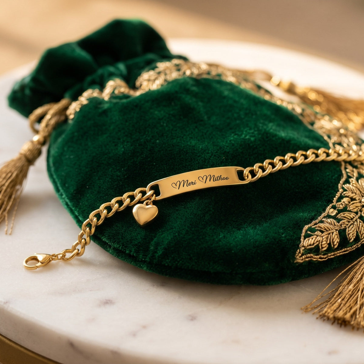Gold heart charm name bracelet on a green velvet potli bag