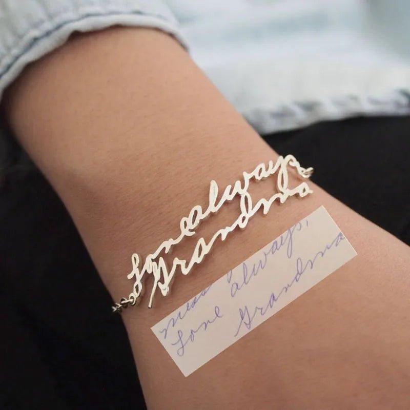 Scripted bracelet: gold-tone chain bracelet cast from actual handwriting, 'Love always Grandma' worn on a wrist, with the handwritten note beside it