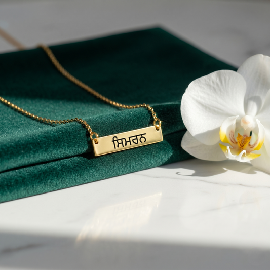 Gold necklace with a nameplate on a green fabric background with a white orchid.