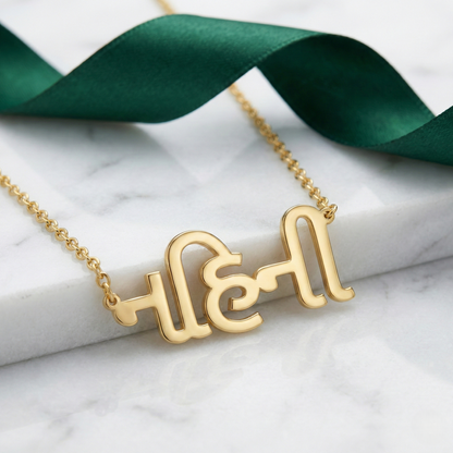 Gujrati_name_necklace Gold necklace with a unique design on a marble surface with green ribbon