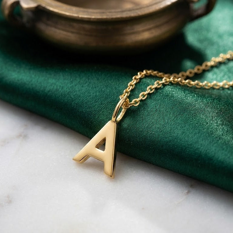 Gold necklace with a 'A' pendant on a green fabric background