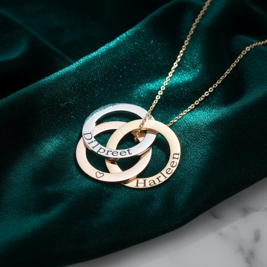 Gold necklace with interlocking rings engraved with names on a green velvet background