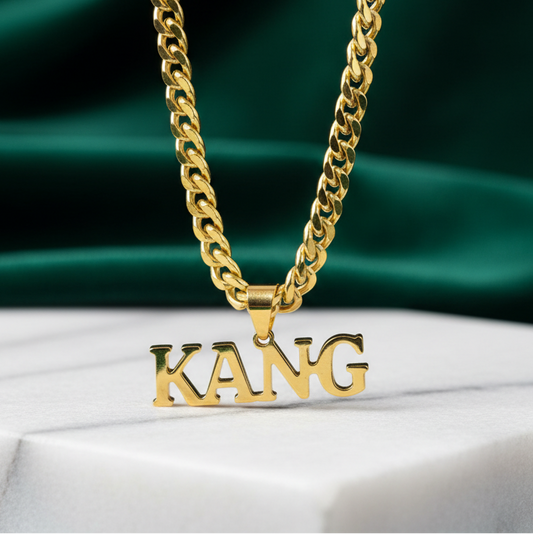 Gold chain necklace with 'KANG' pendant on a green and white fabric background