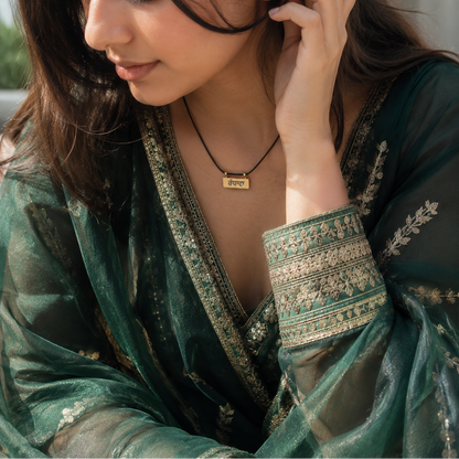 Woman adjusting an earring, wearing a green traditional outfit with intricate patterns.