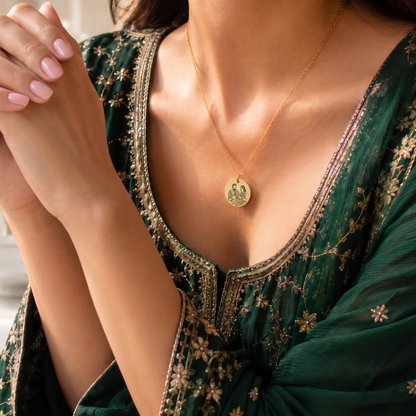 Woman wearing a green embroidered dress with a gold necklace, sitting indoors.