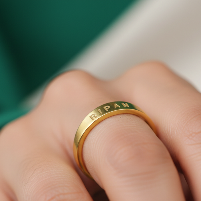 Gold ring with engraved text on a hand against a blurred green and beige background