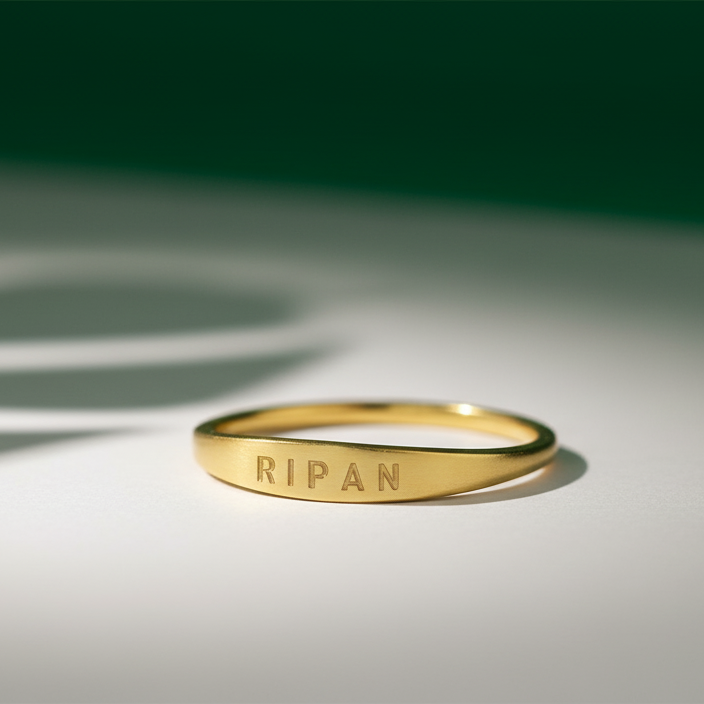 Gold ring with 'RIPAN' engraving on a white surface with green background