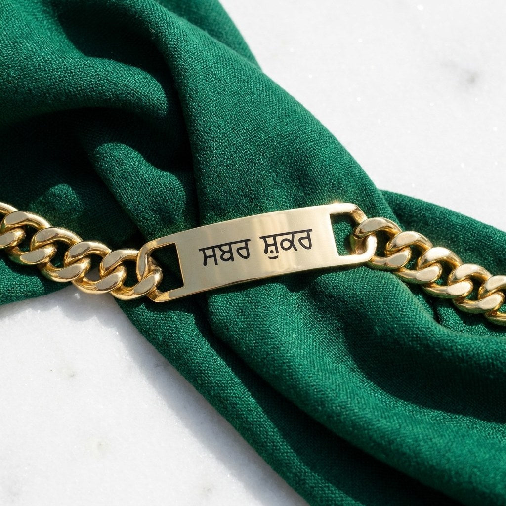 Close view of ਸਬਰ ਸ਼ੁਕਰ engraved on the bar of a gold curb bracelet