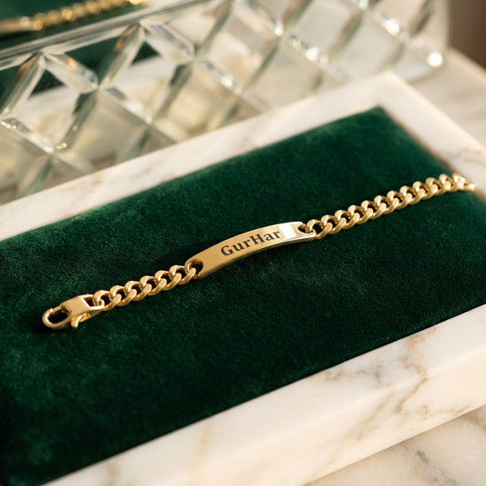 Gold curb name bracelet engraved with GurHar, on green velvet in a marble tray