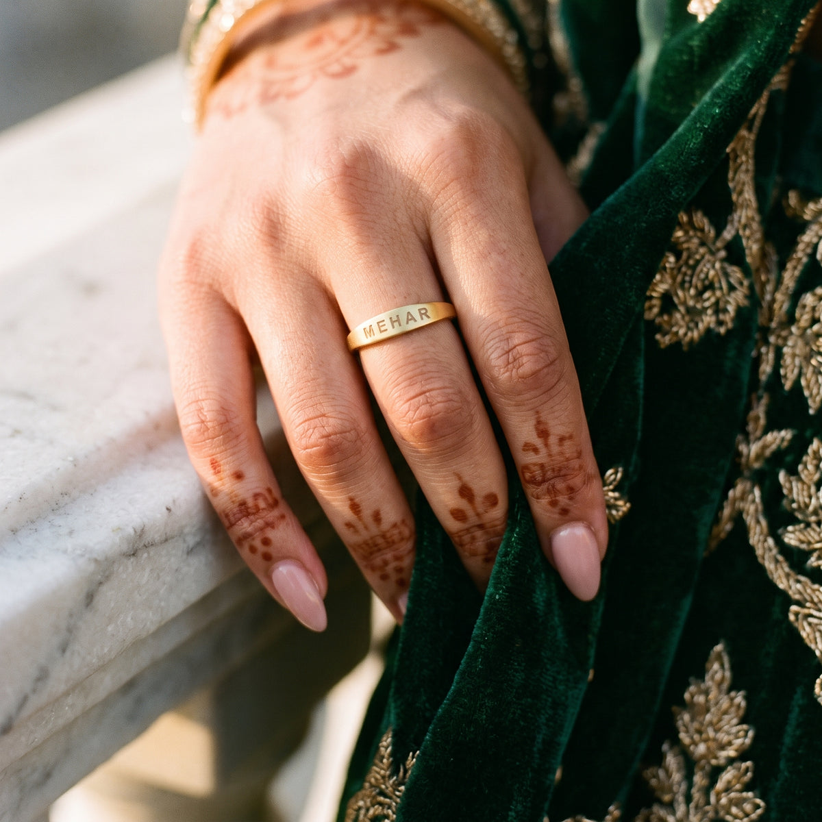 Slim gold name ring engraved MEHAR on a hand with mehndi