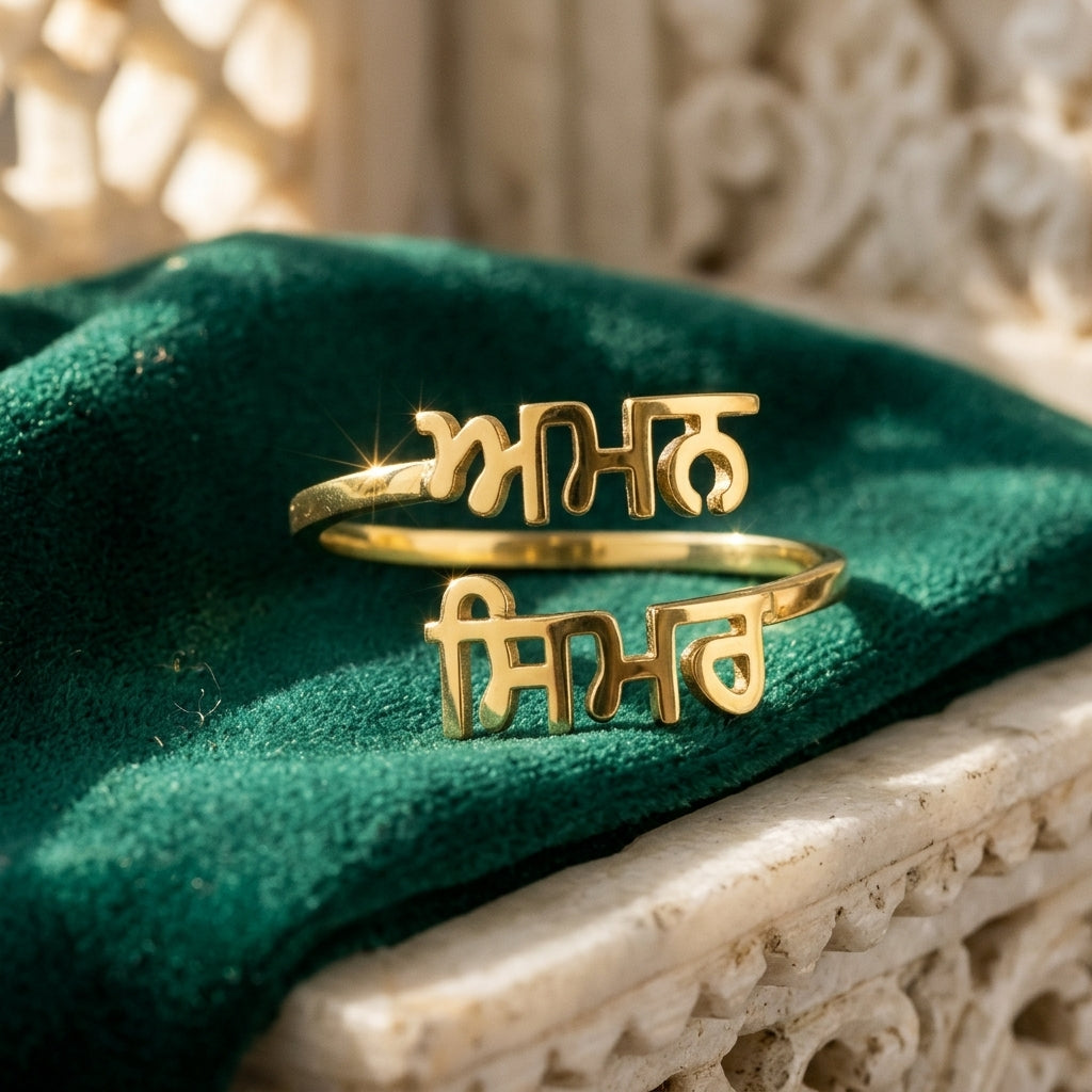 Gold double name ring with Punjabi names Aman and Simar on green velvet