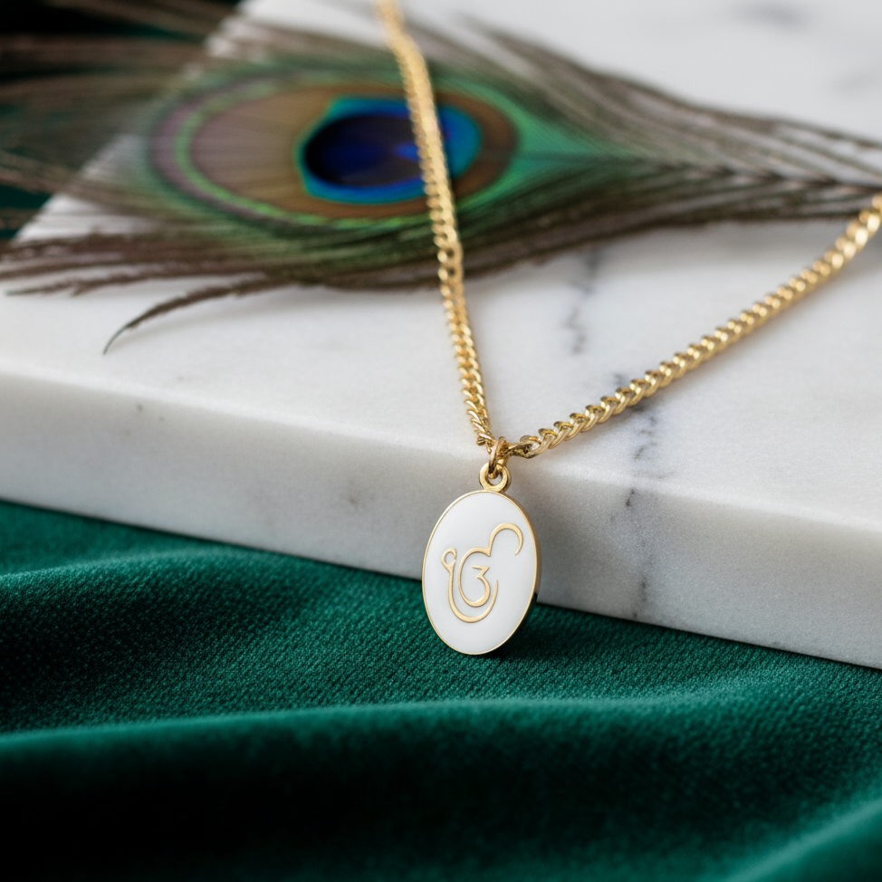 Gold necklace with a white pendant on a marble surface with peacock feathers