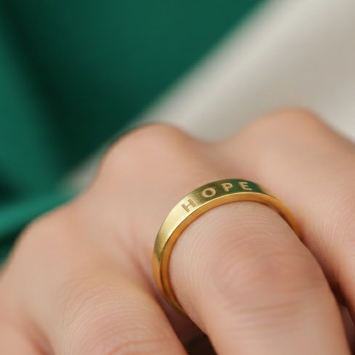 Gold ring with green engraving on a hand against a blurred background