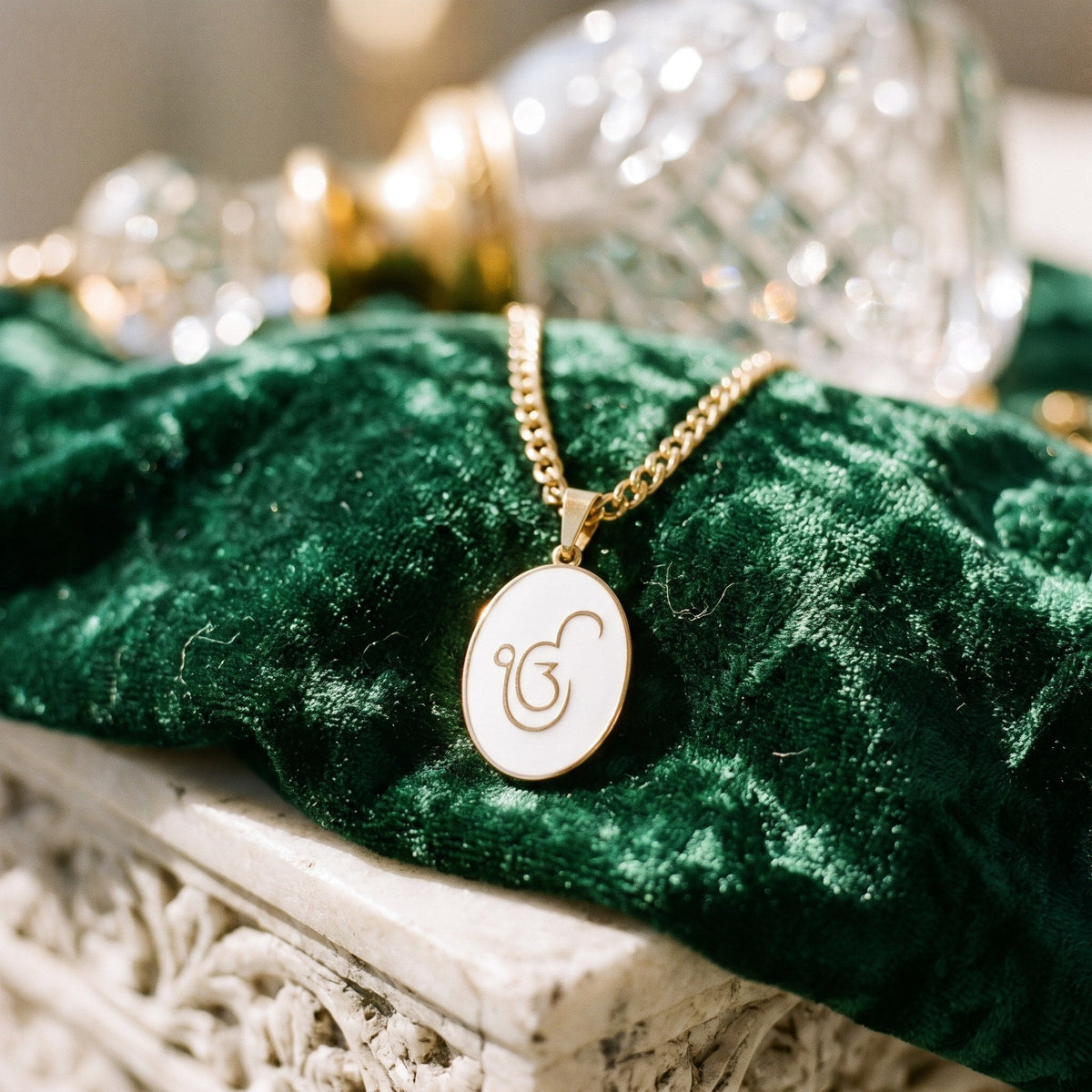 Ik Onkar enamel pendant on green velvet beside a crystal bottle