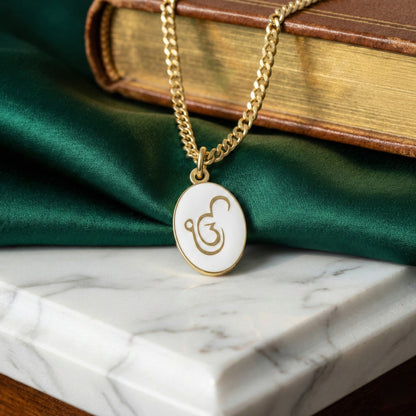 Ik Onkar pendant necklace: gold-plated Ik Onkar on white enamel, on a chain, on marble with a book