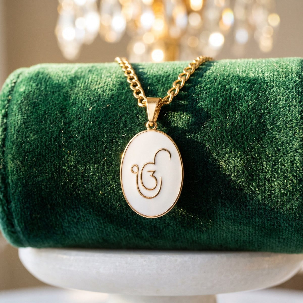 Ik Onkar enamel pendant on a gold curb chain over a green velvet roll