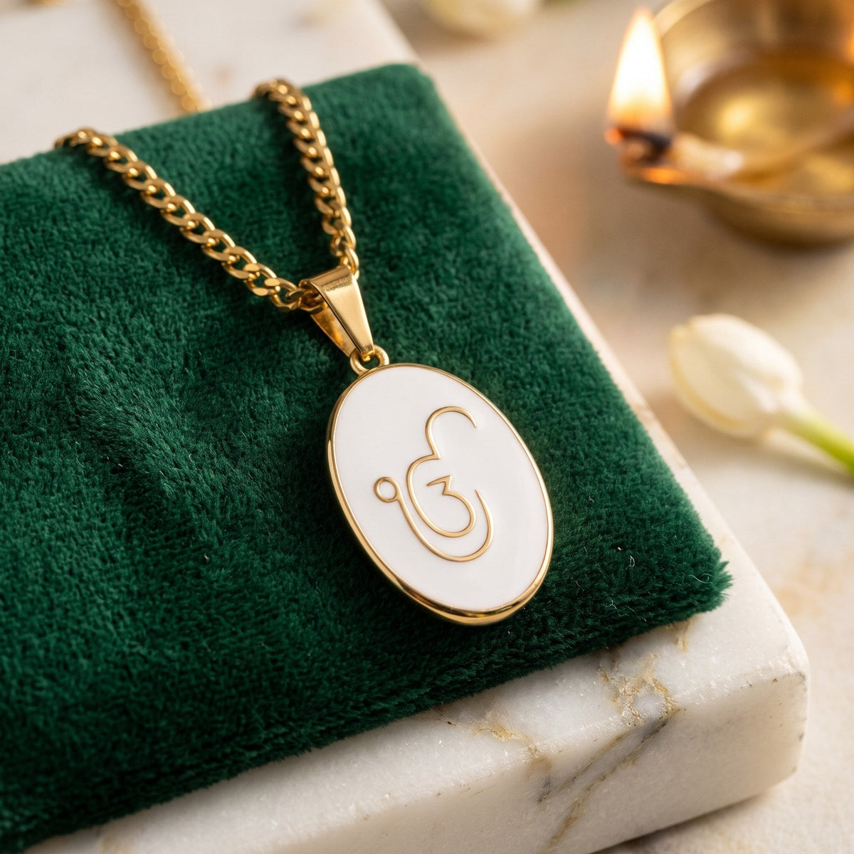 Ik Onkar enamel pendant on green velvet beside a diya