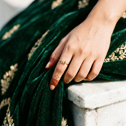 Thin gold initial ring with letter M on a hand resting on green velvet