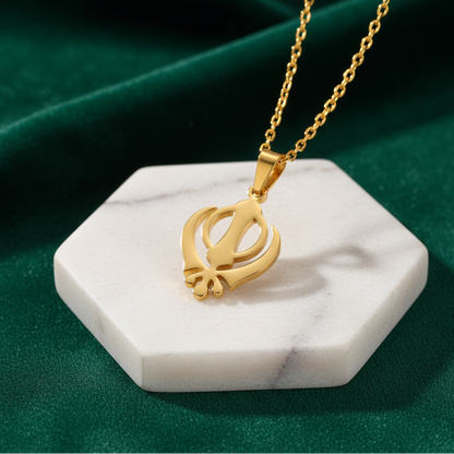 Gold necklace with a pendant on a white marble stand against a green background