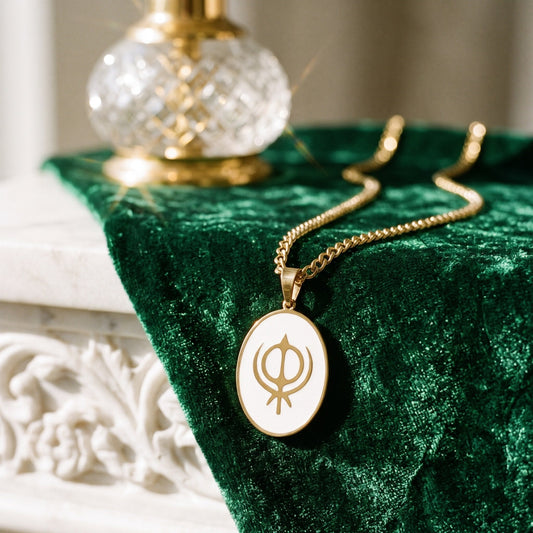 Khanda enamel pendant on green velvet beside a crystal bottle