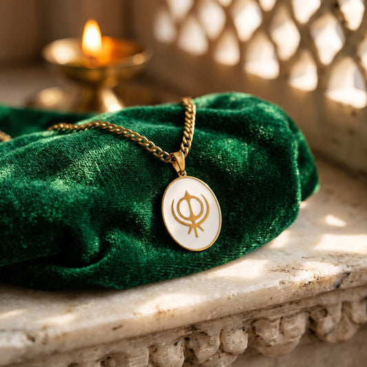 Khanda enamel pendant on green velvet beside a diya