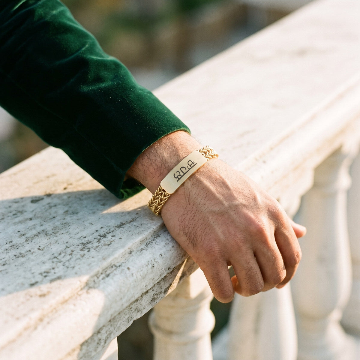 Gold name bracelet on a man's wrist resting on a marble railing