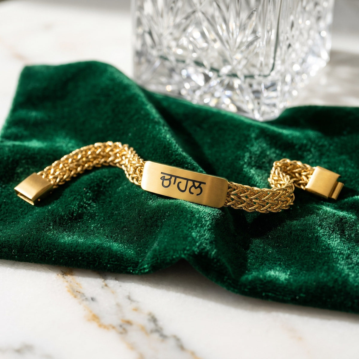 Gold name bracelet with ਚਾਹਲ in Punjabi on green velvet next to a crystal glass