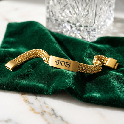 Gold name bracelet with ਚਾਹਲ in Punjabi on green velvet next to a crystal glass