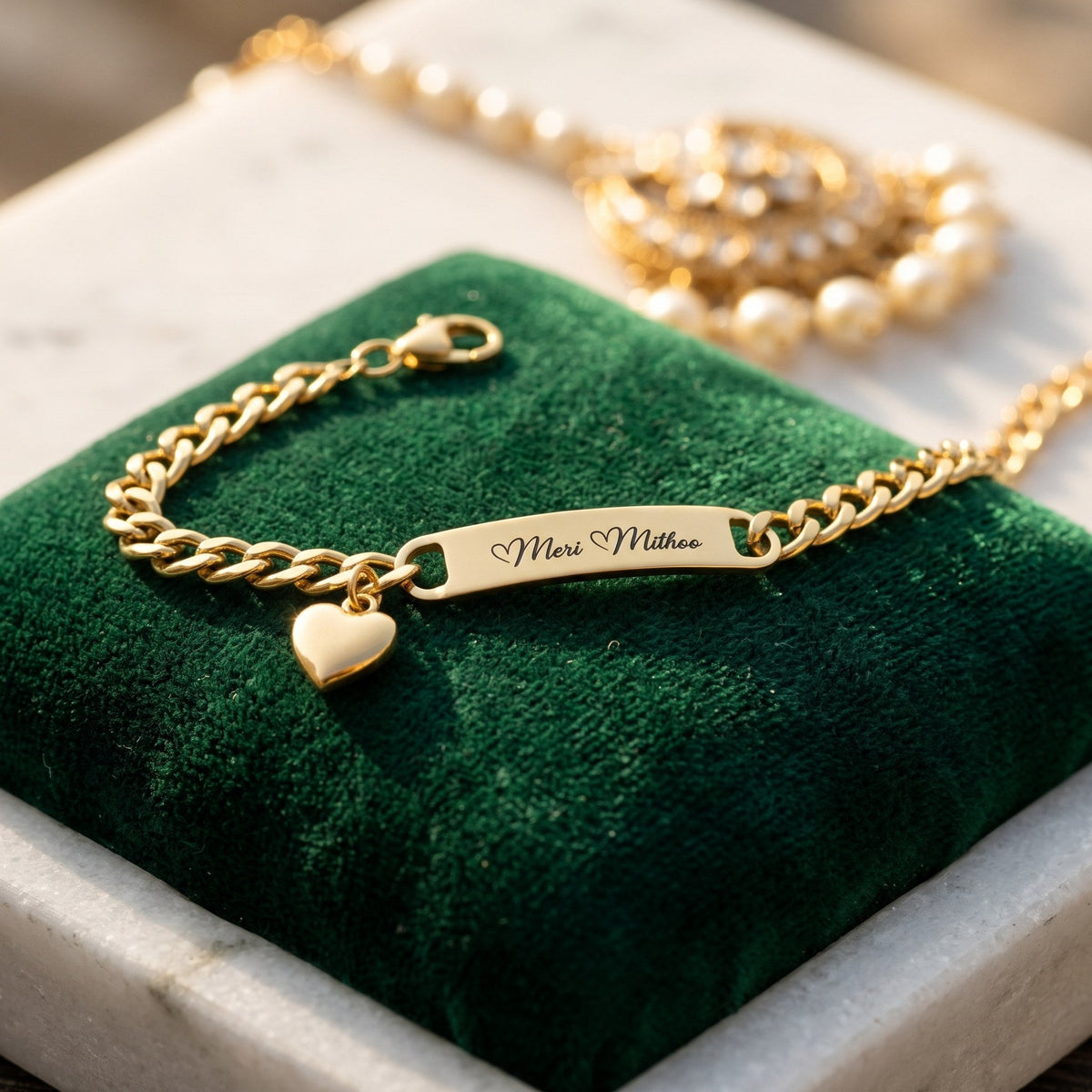 Gold heart charm name bracelet engraved Meri Mithoo, on green velvet beside pearl jewellery