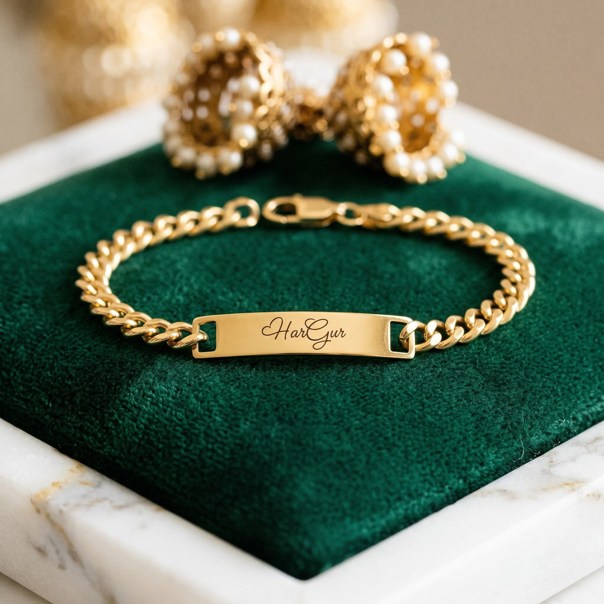 Gold name ID bracelet engraved HarGur in script, on green velvet beside gold jhumkas