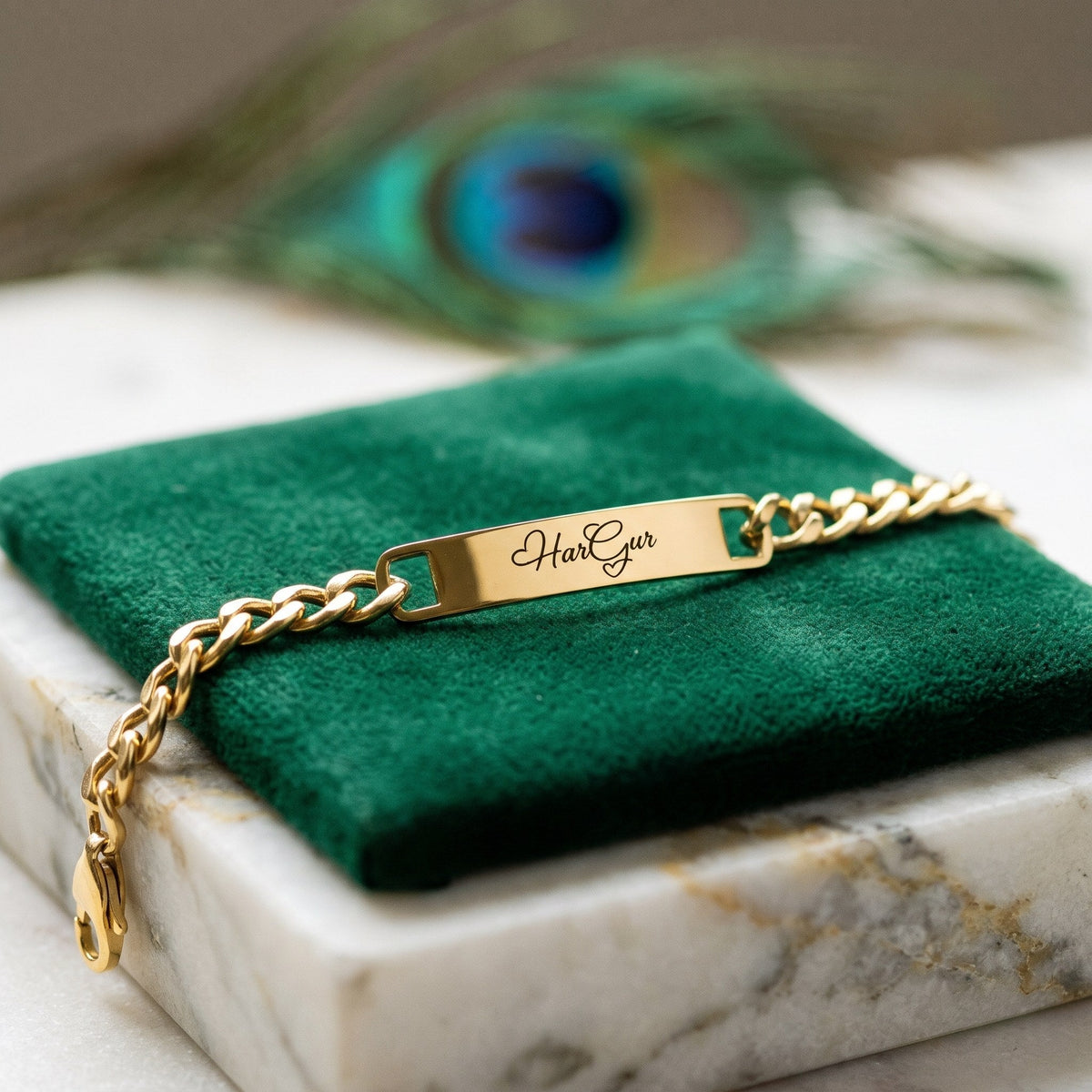 Gold name ID bracelet with HarGur on green velvet, a peacock feather behind
