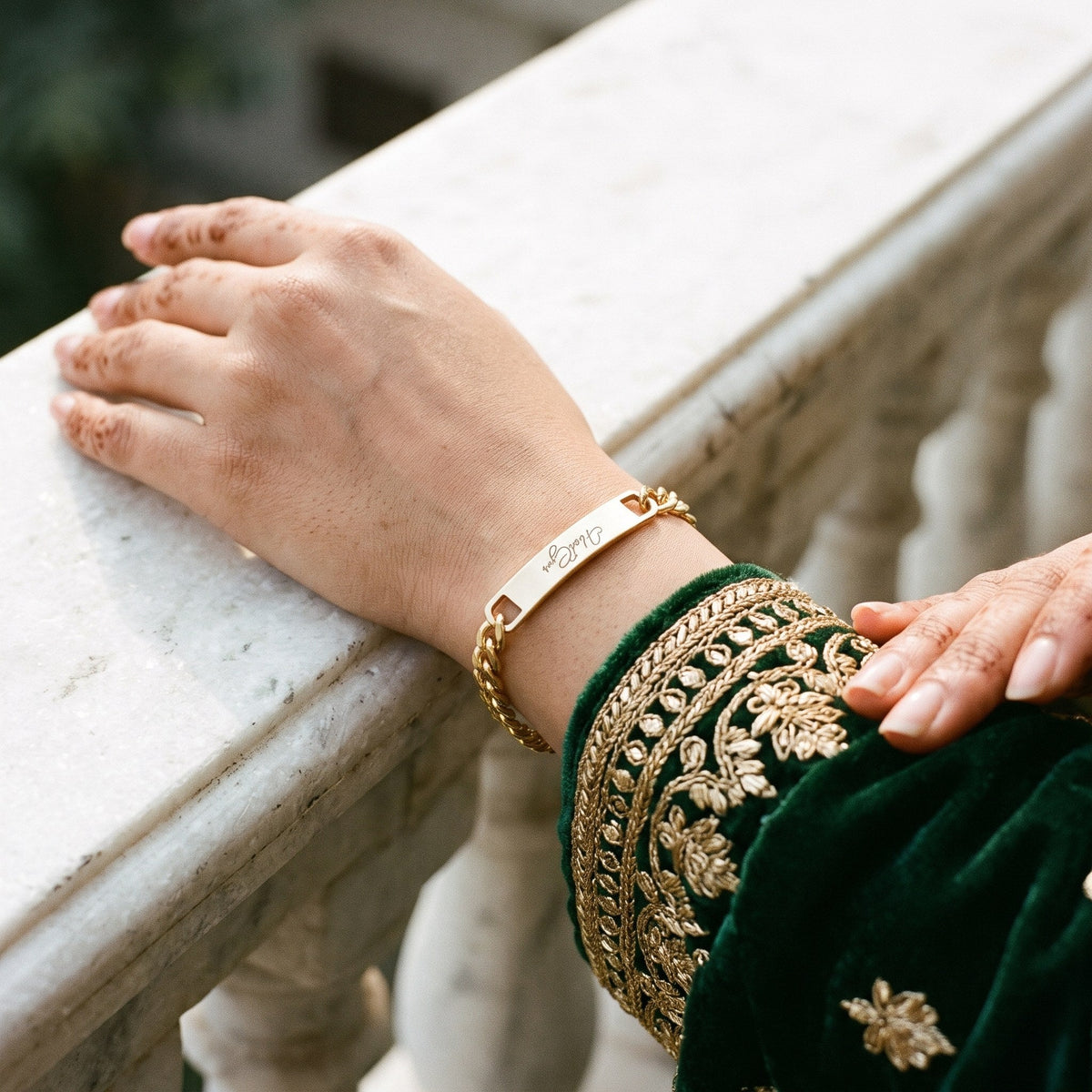 Gold name ID bracelet on a woman's wrist with an embroidered green sleeve