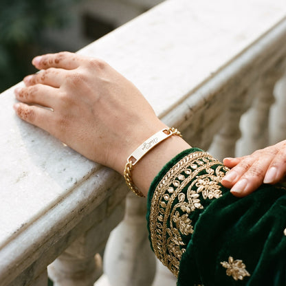 Gold name ID bracelet on a woman's wrist with an embroidered green sleeve